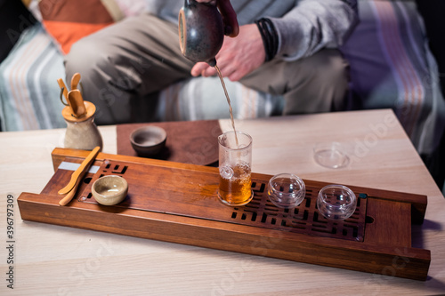 A man passes hot amber tea from a glass flask into a cup. To preserve its strong flavor. Bamboo tray gongfu close-up
