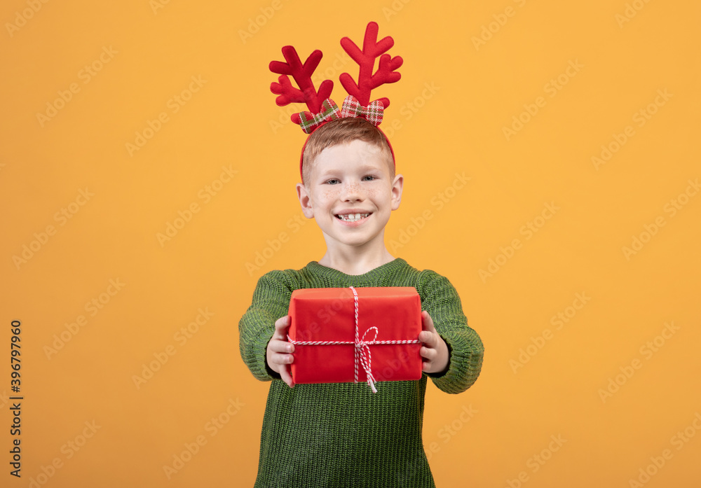 Smiling boy giving Christmas gift over yellow background Smiling boy giving Christmas gift over yellow background