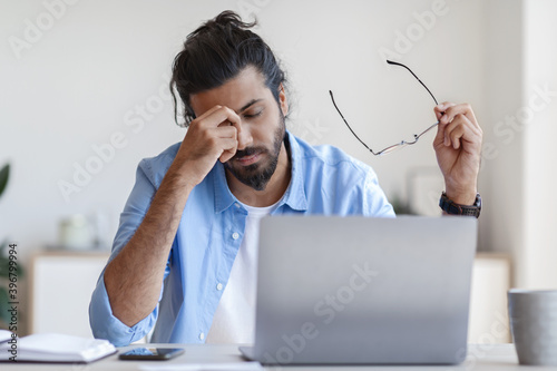 Eyes Fatigue. Young freelancer guy massaging nosebridge, tired after working on laptop photo