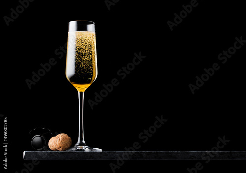 Elegant glass of yellow champagne with cork and wire cage on black marble board on black background. Space for text