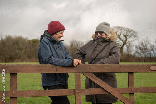 Two female friends talking outdoors leaning on a wooden fence