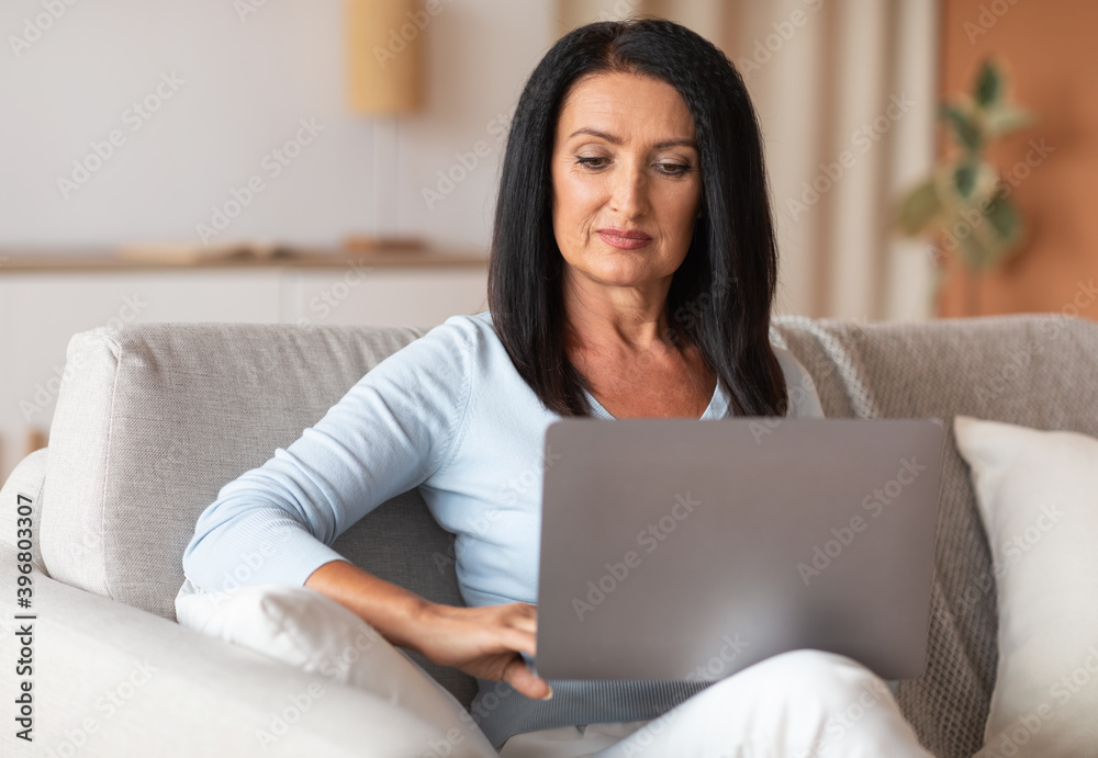 Mature woman sitting on couch and working on computer Mature woman sitting on couch and working on computer