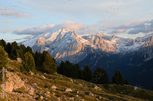 Beautiful orange montain sunset in the alps of South Tyrol with the peaks covered by first snow during autumn and a forest in the foreground
