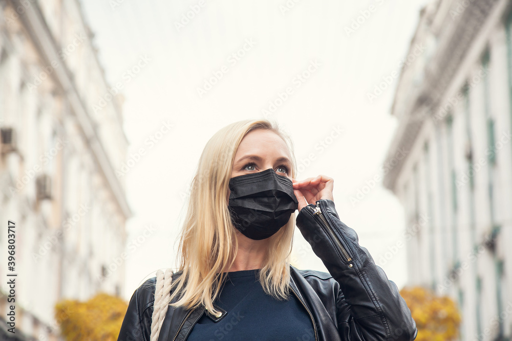 Fototapeta premium Woman in the background of the city wants to remove a black protective face mask