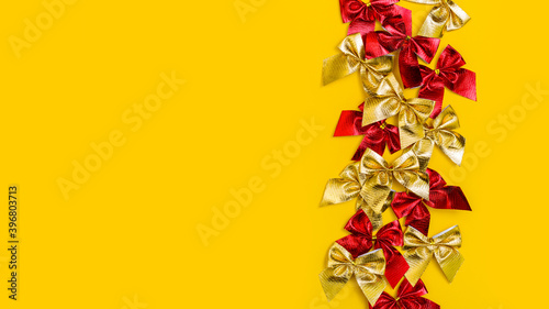holiday background: red and gold shiny bows on yellow background, copy space