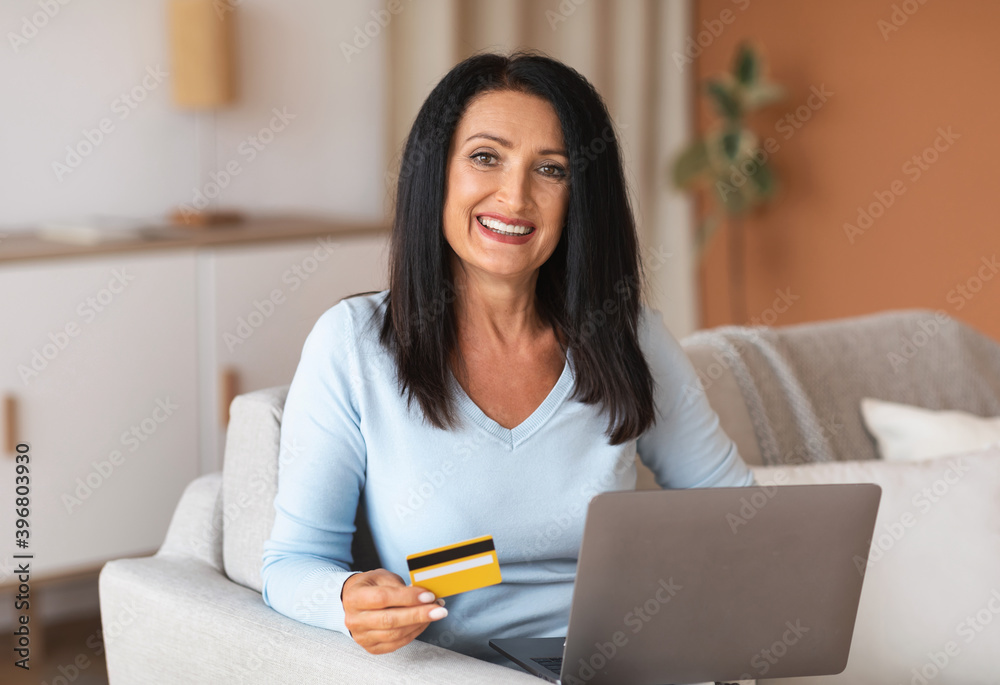 Fototapeta premium Mature woman making purchases using laptop holding card
