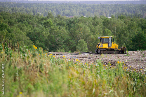 Yellow tractor on landfill near green forest. Waste sorting and preparation for recycling. Caring for environment.