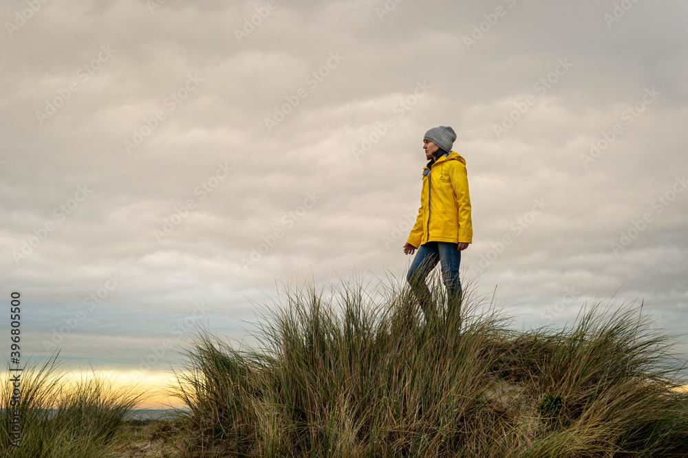 Woman wearing a yellow coat standing on top of a dune Woman wearing a yellow coat standing on top of a dune