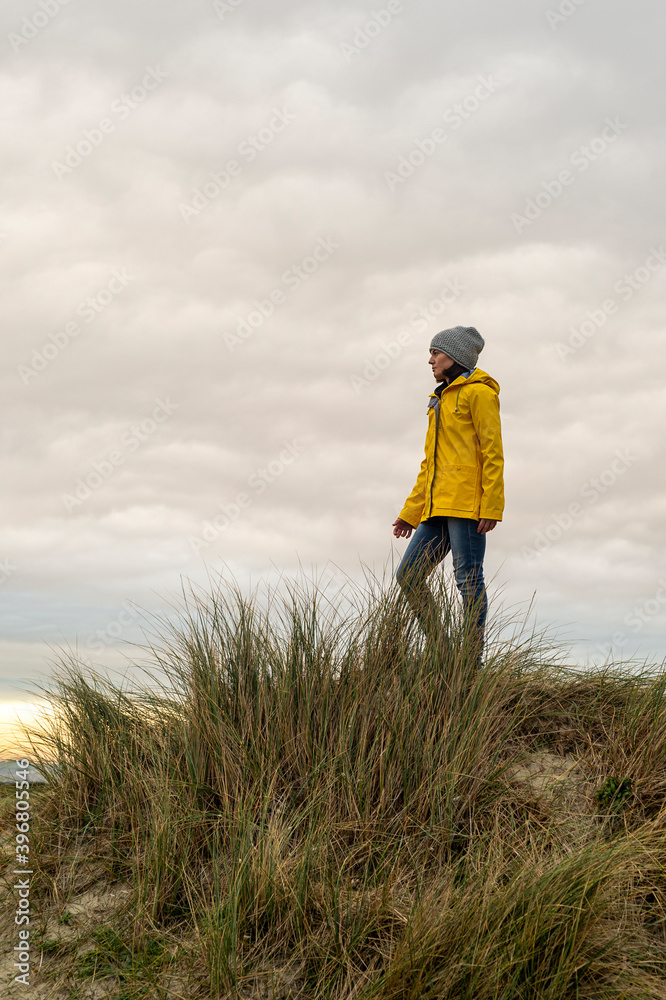 woman wearing a yellow coat standing on top of a dune