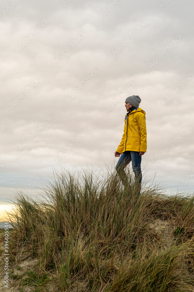 woman wearing a yellow coat standing on top of a dune woman wearing a yellow coat standing on top of a dune