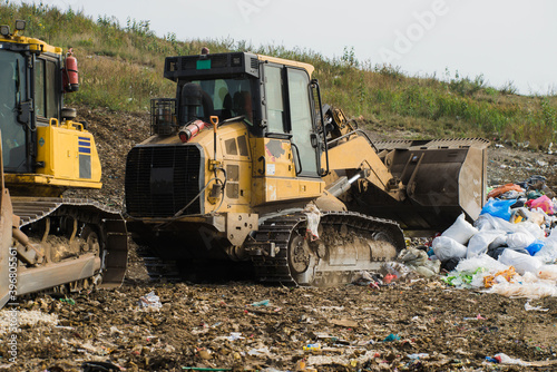 Yellow tractors. Pile of household garbage. Waste sorting and preparation for recycling on landfill. Caring for environment.