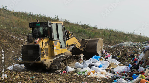 Yellow tractor works on dump. Household garbage. Waste sorting on landfill of big city. Preparation for recycling.