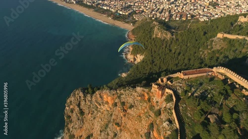 Parachute jumper is flying over beautiful panorama of sunny Alanya town, famous Fortress and mountains overwashed by Mediterranean sea. Drone footage, 4k. photo