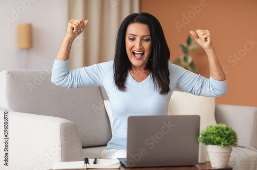 Excited mature woman screaming yes using laptop