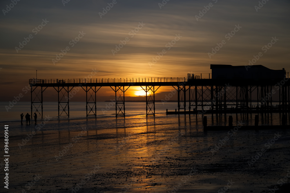 A beautiful moody sunset with reflections in the water and sand be the Pier at Bognor Regis.