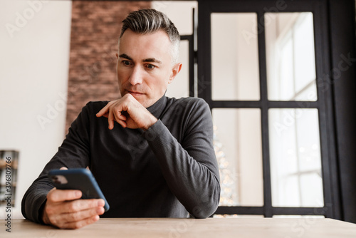 Handsome focused man using mobile phone while sitting at home