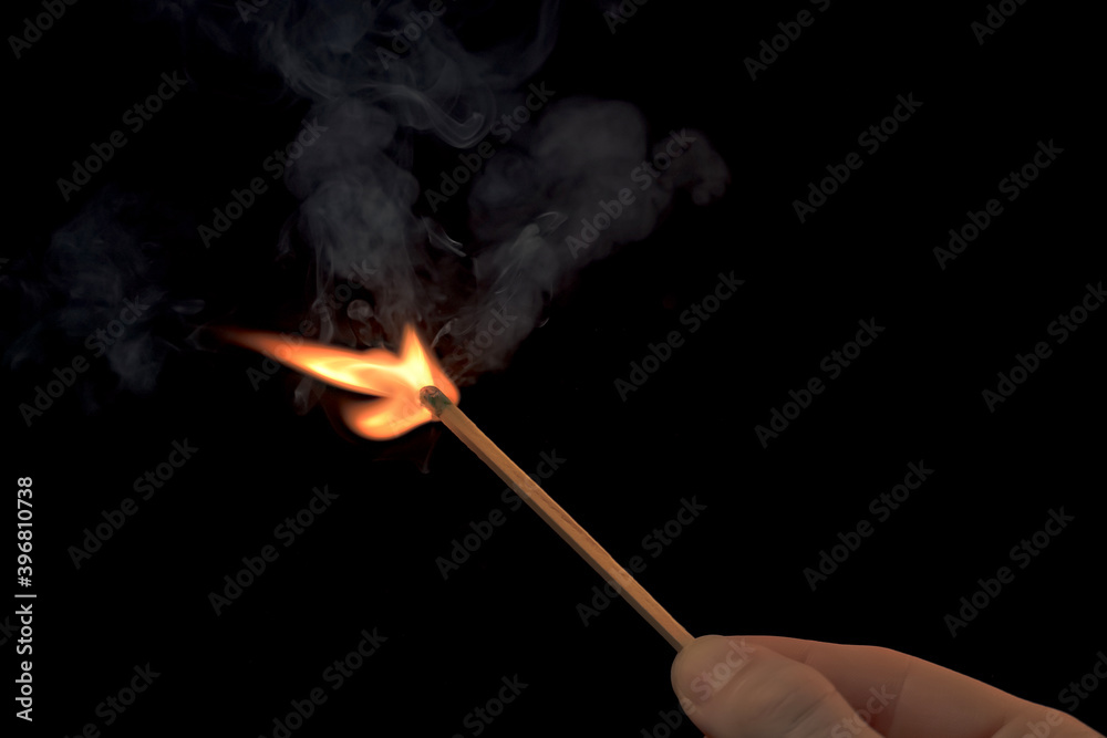 Hand holding a lighted match with fire flame and smoke on a black background.