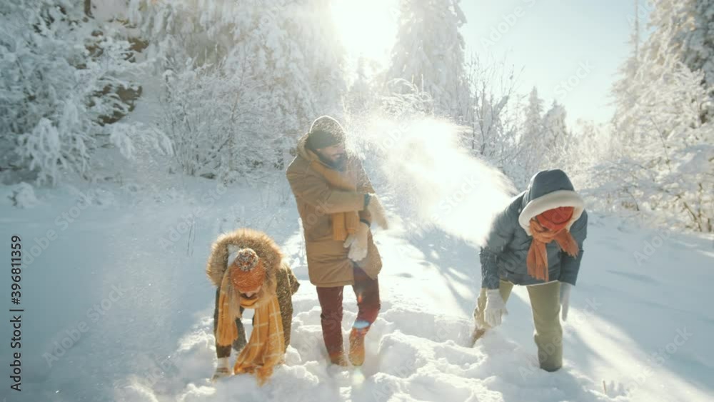 Group of young excited male and female friends playing snowballs and throwing snow in forest while having fun outdoors on sunny winter day
