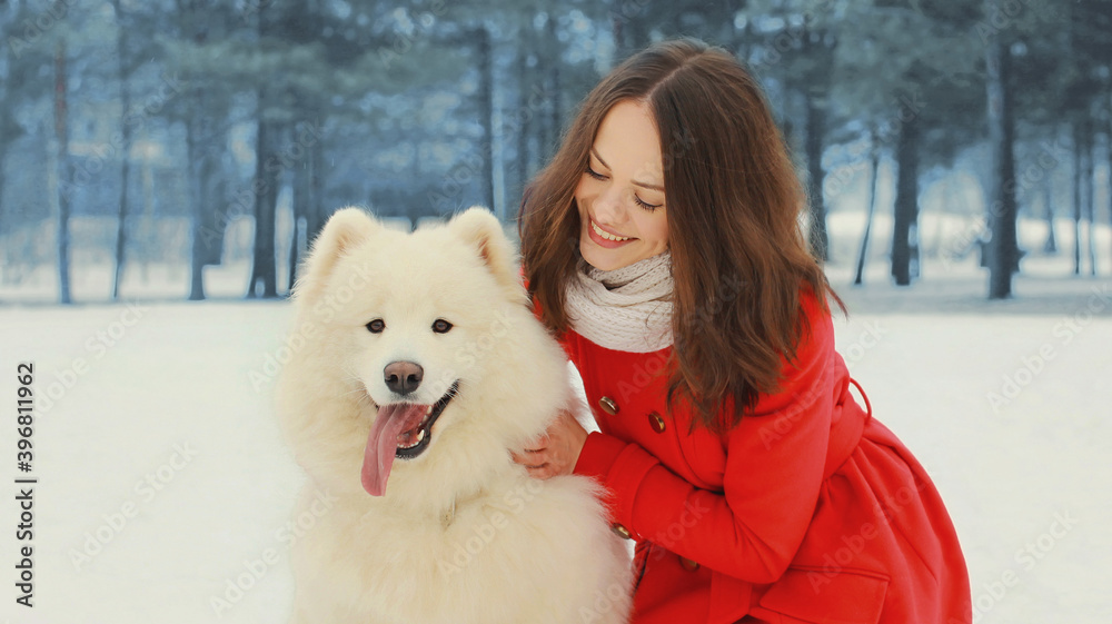Portrait of beautiful smiling young woman owner with white Samoyed dog in winter park