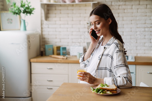 Happy pregnant woman talking on cellphone while having breakfast