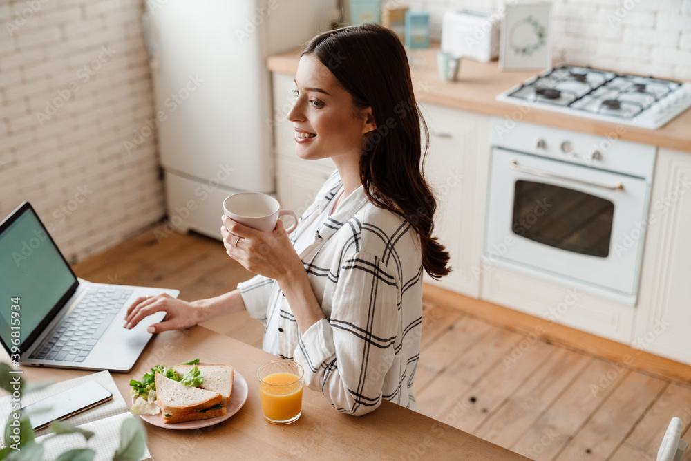Beautiful smiling woman working with laptop while having breakfast Beautiful smiling woman working with laptop while having breakfast