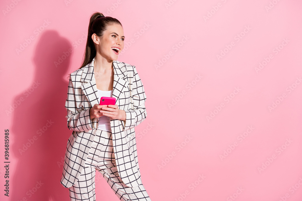 Photo portrait of laughing girl holding phone in two hands looking at blank space isolated on pastel pink colored background Photo portrait of laughing girl holding phone in two hands looking at blank space isolated on pastel pink colored background