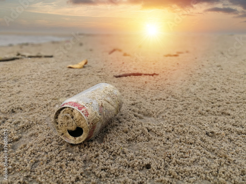 Used beverage can that become garbage on the beach with sunset sky, Environmental pollution concept.