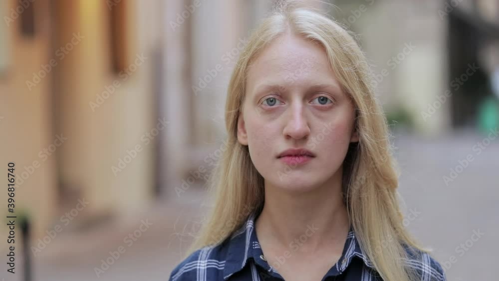 Portrait of beautiful young woman looking to camera. Crop view of blond hair woman wearing blue plaid shirt while standing at old european city street. Concept of headshot. Zoom in. Portrait of beautiful young woman looking to camera. Crop view of blond hair woman wearing blue plaid shirt while standing at old european city street. Concept of headshot. Zoom in.