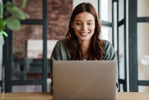 Beautiful smiling woman working with laptop while sitting at table photo