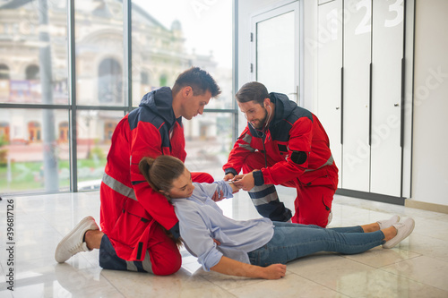 Two medical workers in red uniform halping a faint woman photo