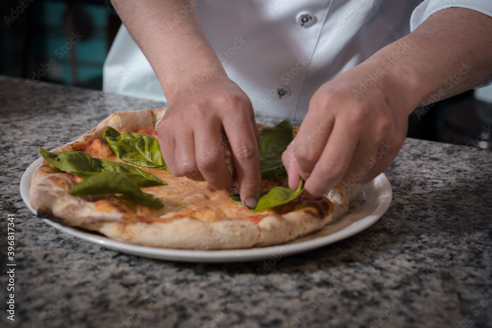 hands of the chef decorating handmade pizza with basil leaves
