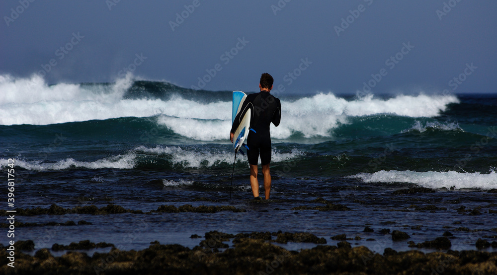 Young man entering the water through the stones to surf, with a surfboard. Young man entering the water through the stones to surf, with a surfboard.