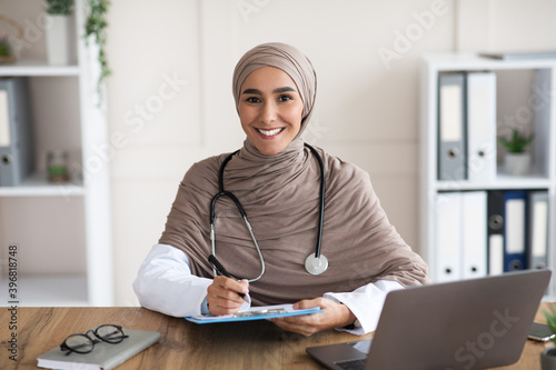 Smiling woman doctor in hijab taking anamnesis in clinic