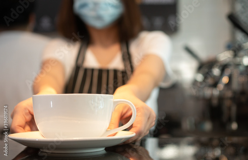 Asian waitress woman wearing face masks To prevent contagious diseases And is holding coffee cups to serve customers in the coffee shop. The concept of safety and prevention from COVID 19 outbreak
