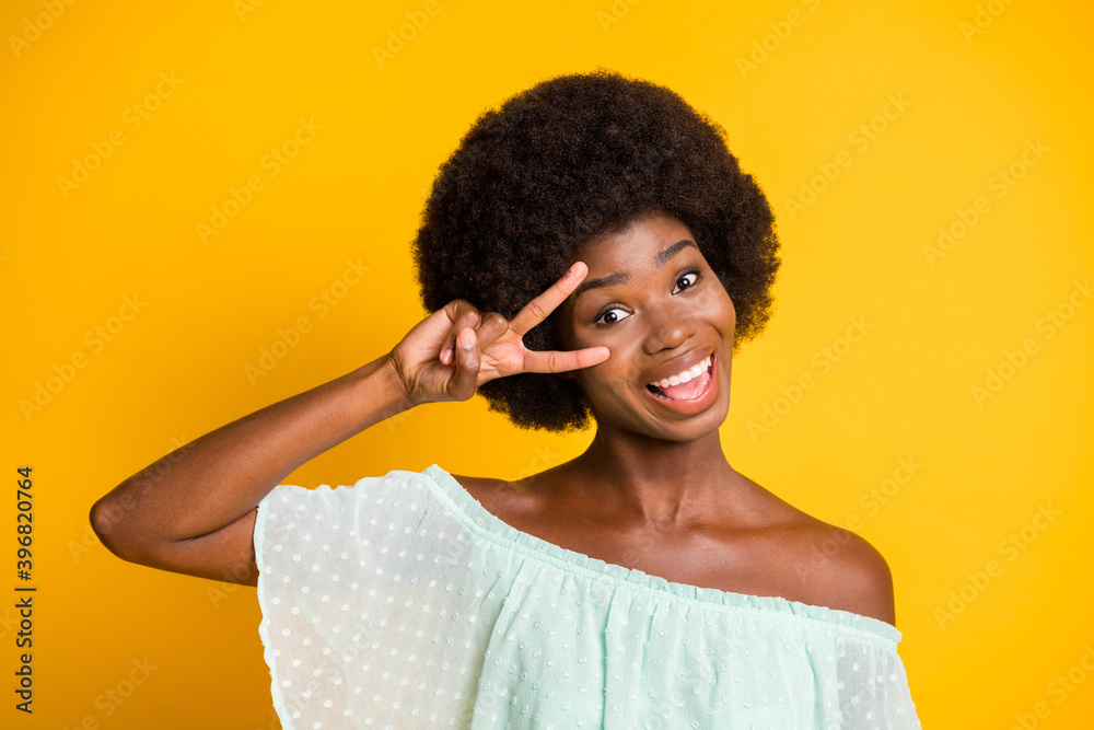 Photo portrait of woman saying hi holding v-sign near eye isolated on vivid yellow colored background Photo portrait of woman saying hi holding v-sign near eye isolated on vivid yellow colored background