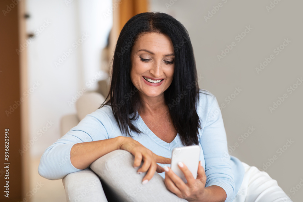 Smiling mature lady using smartphone at her home Smiling mature lady using smartphone at her home