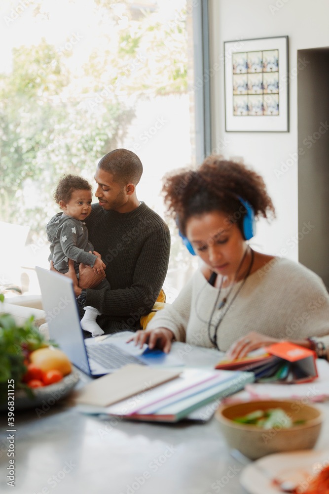 Father holding baby daughter behind working mother at laptop Father holding baby daughter behind working mother at laptop