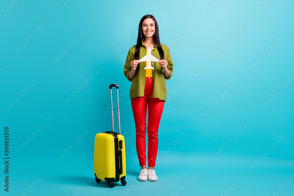 Full length photo of girl hold big case paper plane beaming smile wear green shirt trousers sneakers isolated blue color background Full length photo of girl hold big case paper plane beaming smile wear green shirt trousers sneakers isolated blue color background
