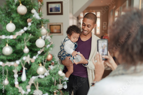 Woman photographing husband and baby daughter at Christmas tree