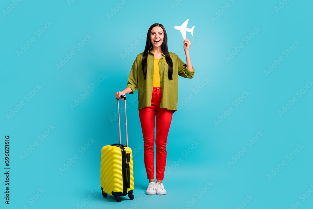 Full length photo of girl hold big case paper plane open mouth wear green shirt pants sneakers isolated blue color background Full length photo of girl hold big case paper plane open mouth wear green shirt pants sneakers isolated blue color background