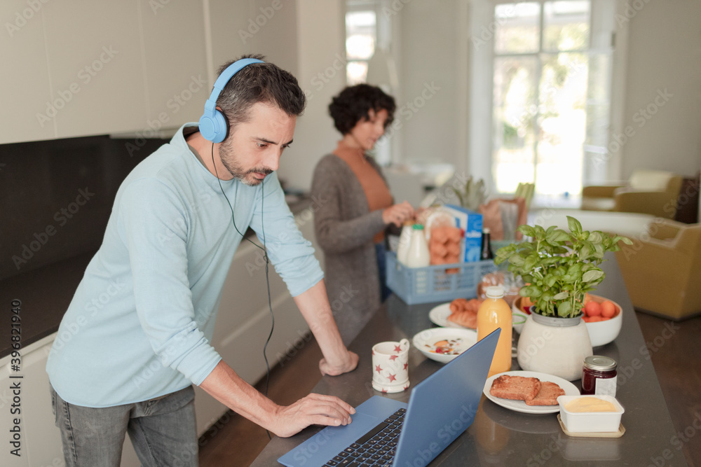 Man with headphones working from home at laptop in kitchen Man with headphones working from home at laptop in kitchen