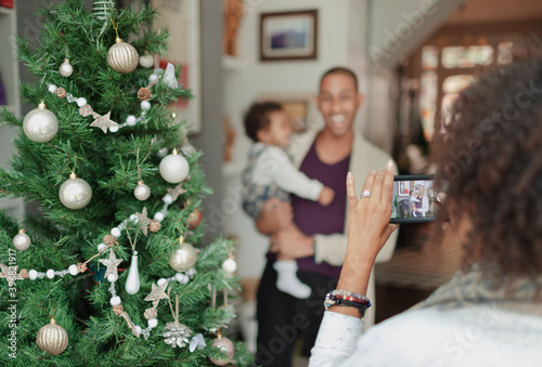 Woman photographing husband and baby daughter by Christmas tree photo