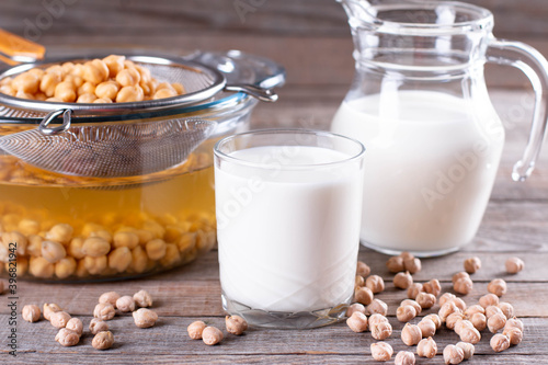 Chickpea vegetarian milk in a jug and a glass  raw chickpeas in bowl on a table. Non-dairy lactose free milk.