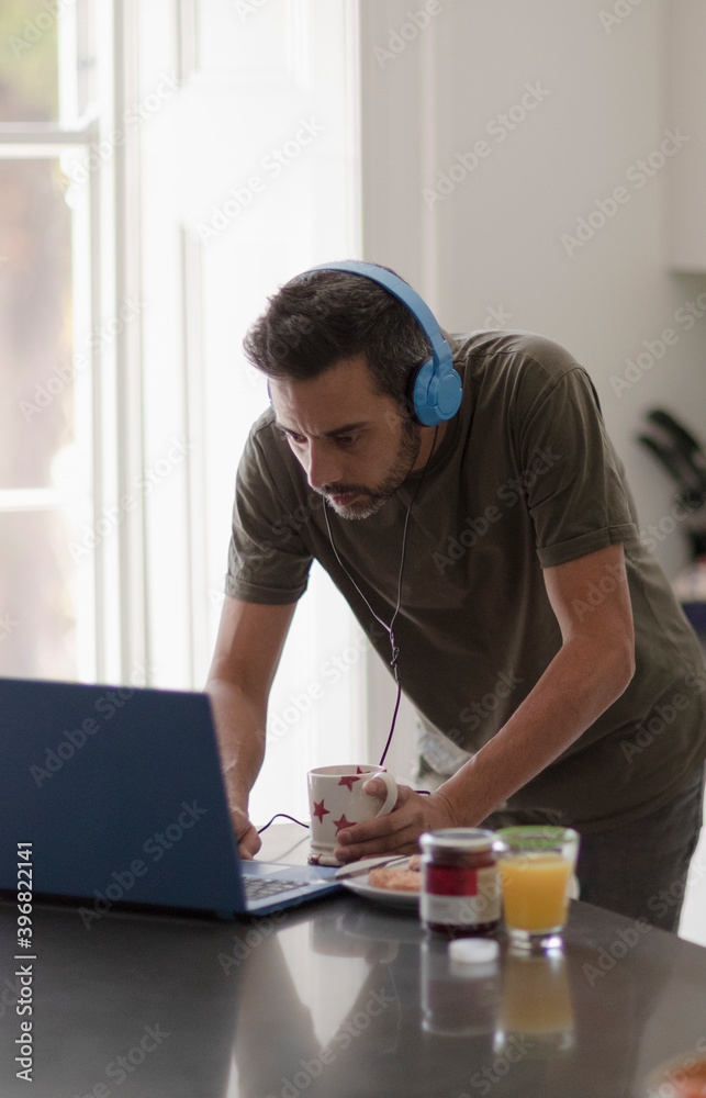 Man with headphones working from home at laptop in kitchen Man with headphones working from home at laptop in kitchen
