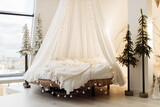 Photo of canopy bed with soft blanket and light garland, near little Christmas tree. Cozy decorated bedroom. Prepare to winter holidays, xmas background, interior design concept
