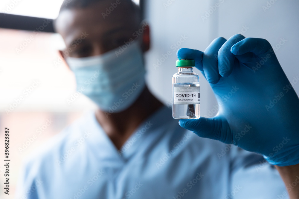 Mixed race male doctor holding covid-19 vaccination wearing face mask and gloves Mixed race male doctor holding covid-19 vaccination wearing face mask and gloves