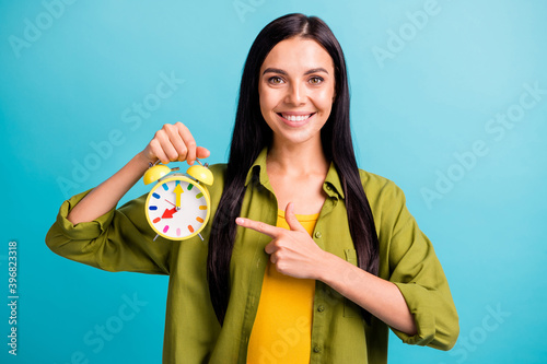 Photo of lady hold alarm clock indicate forefinger shiny smile wear green shirt isolated blue color background