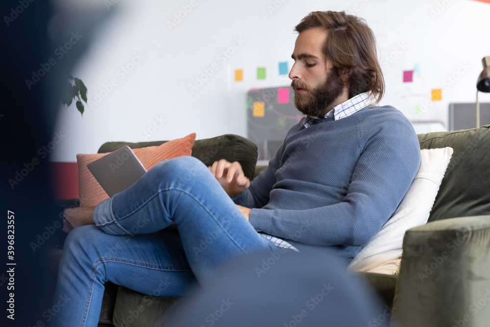 Obraz premium Caucasian businessman using laptop sitting on sofa in creative office
