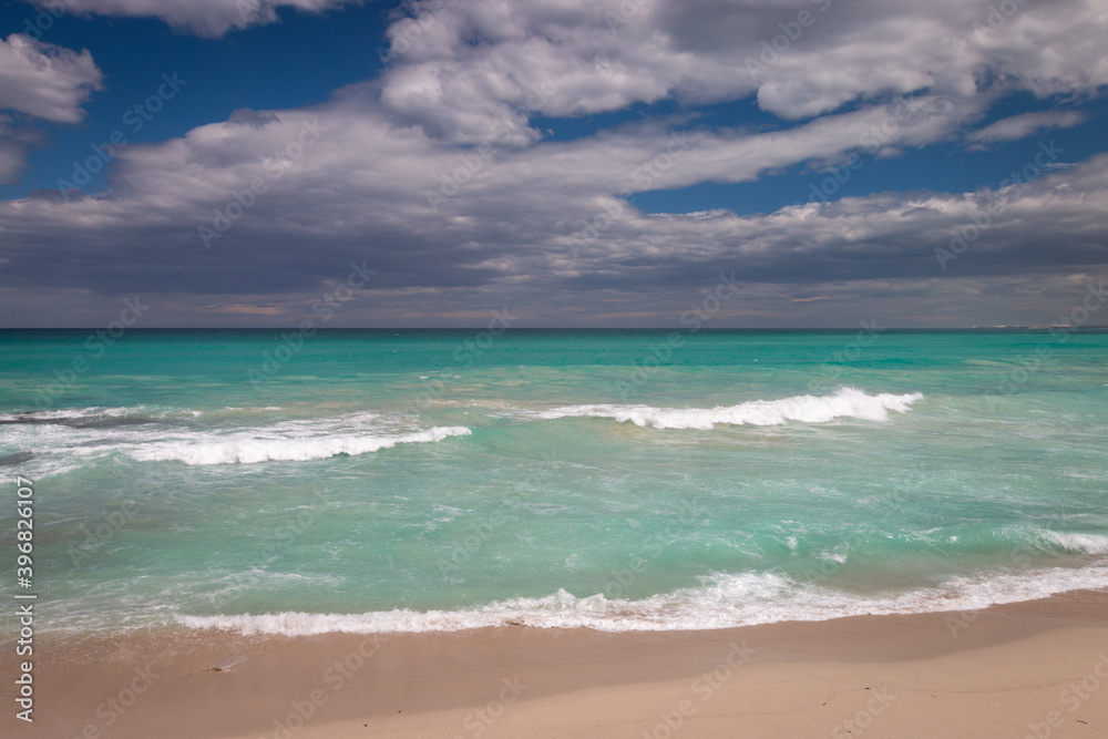 Beach with turquoise colored water against blue sky with clouds.