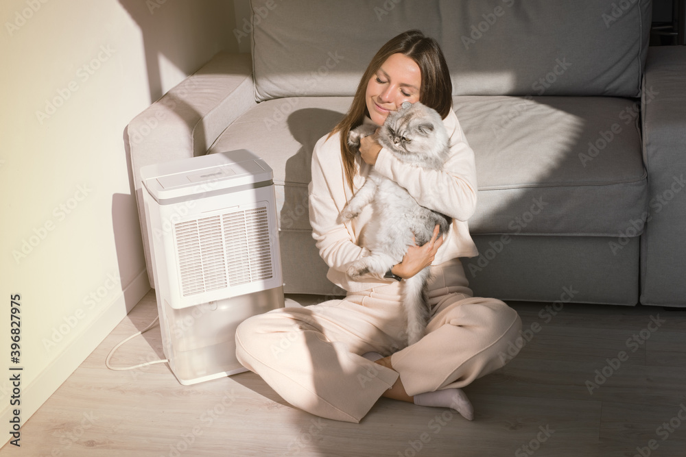 Woman with her cat breathing fresh air at home. Air purifier or